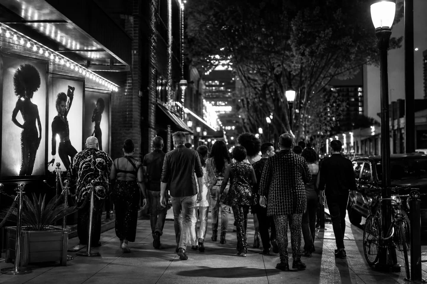 Diverse adults walking through a lively black-and-white nightlife district.