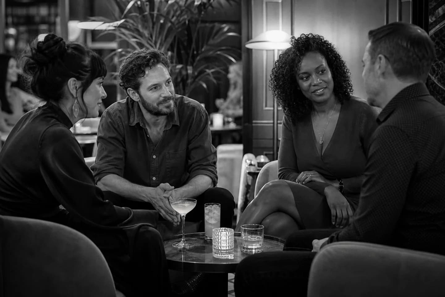 Four fully clothed adults having a relaxed conversation in a monochrome lounge.